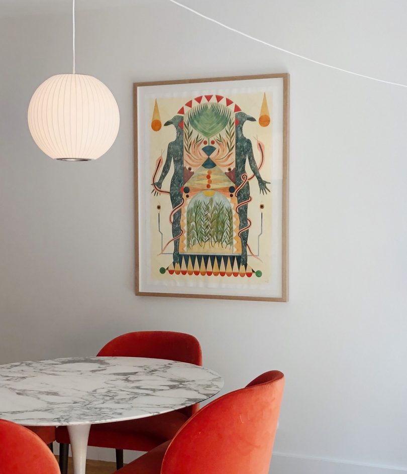 framed colorful symmetrical artwork hanging on white wall in front of dining set
