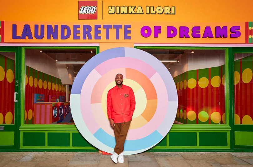 designer Yinka Ilori standing in front of LEGO exhibition exterior in red jacket