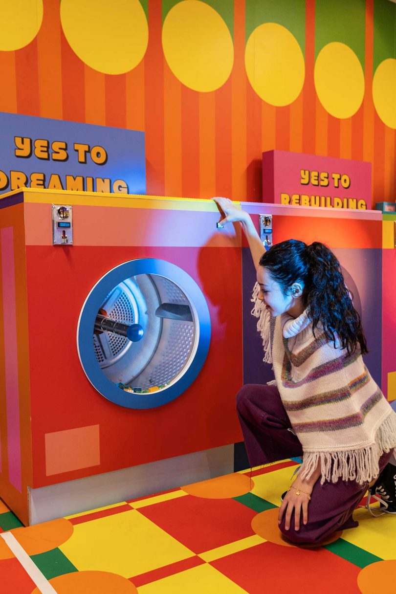 young girl sitting in front of play washing machine in colorful LEGO installation
