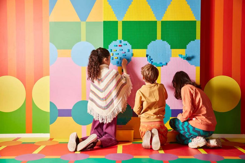 three kids playing with LEGO bricks on colorful wall