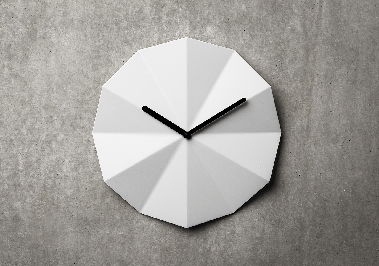 Delta white composite clock by LAWA Designs hung on a cement wall
