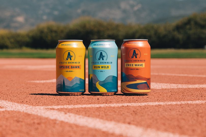 three cans of Athletic alcohol free beer in a row on a tennis court