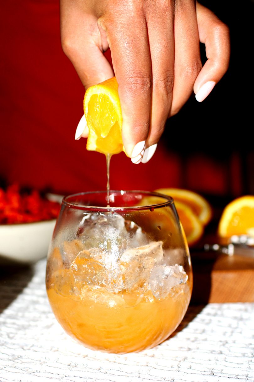 hand squeezing citrus fruit into a glass with ice and an orange liquid