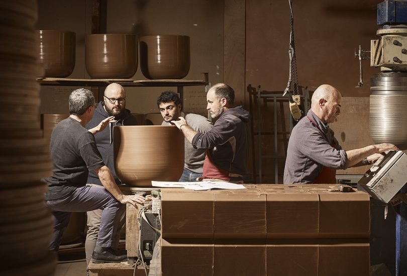 five light skinned men gathered around a large piece of pottery in a studio