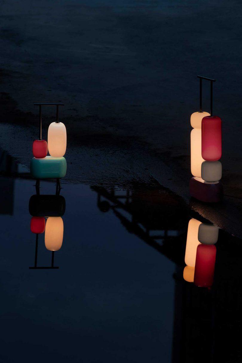 two sculptural colorful lamps turned on against a dark reflective background