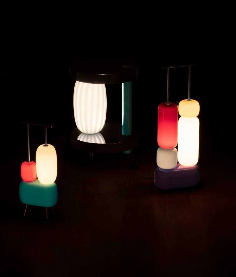 three sculptural colorful lamps turned on against a dark background