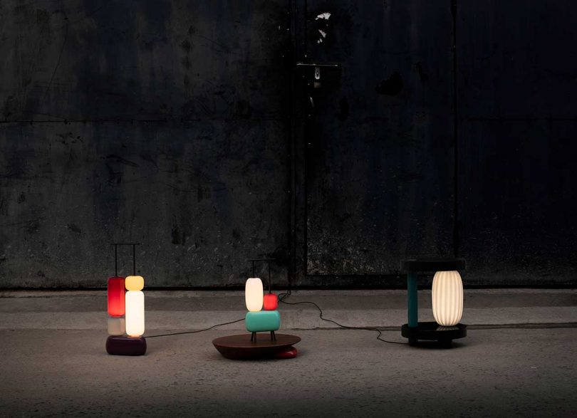 three sculptural colorful lamps turned on against a dark background