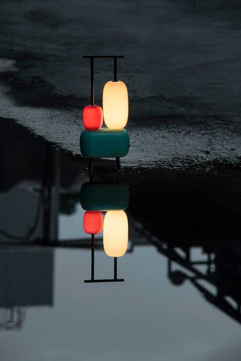 sculptural colorful lamp turned on against a dark reflective background