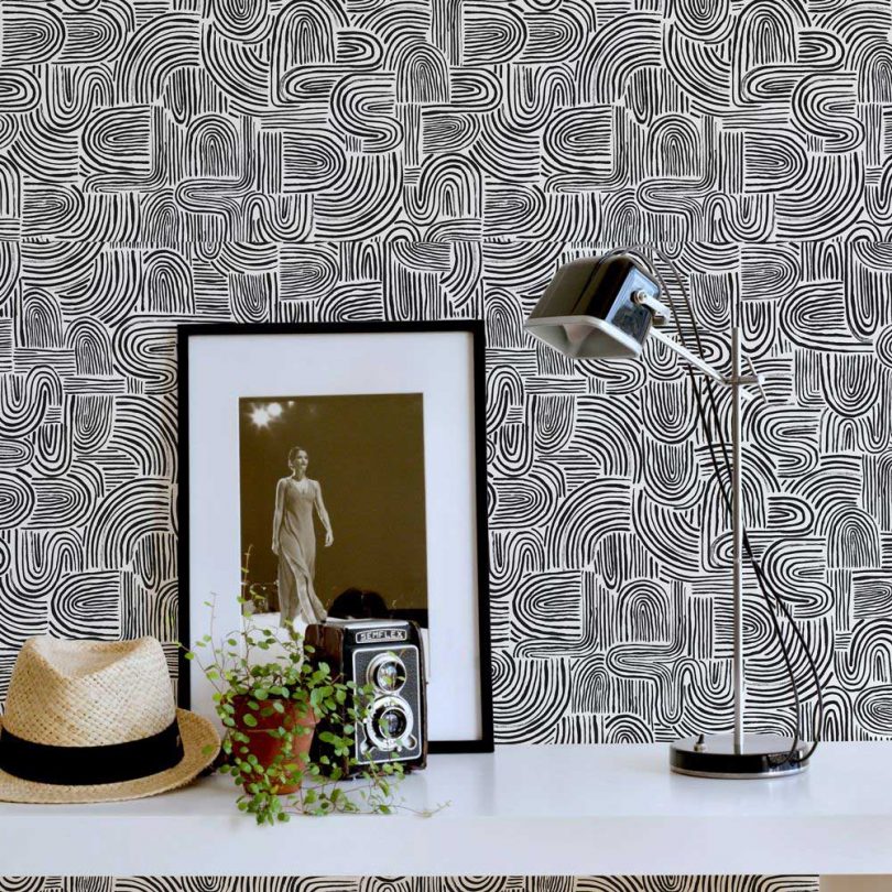 graphic black and white wallpaper with swirls with console table featuring lamp, photo and camera