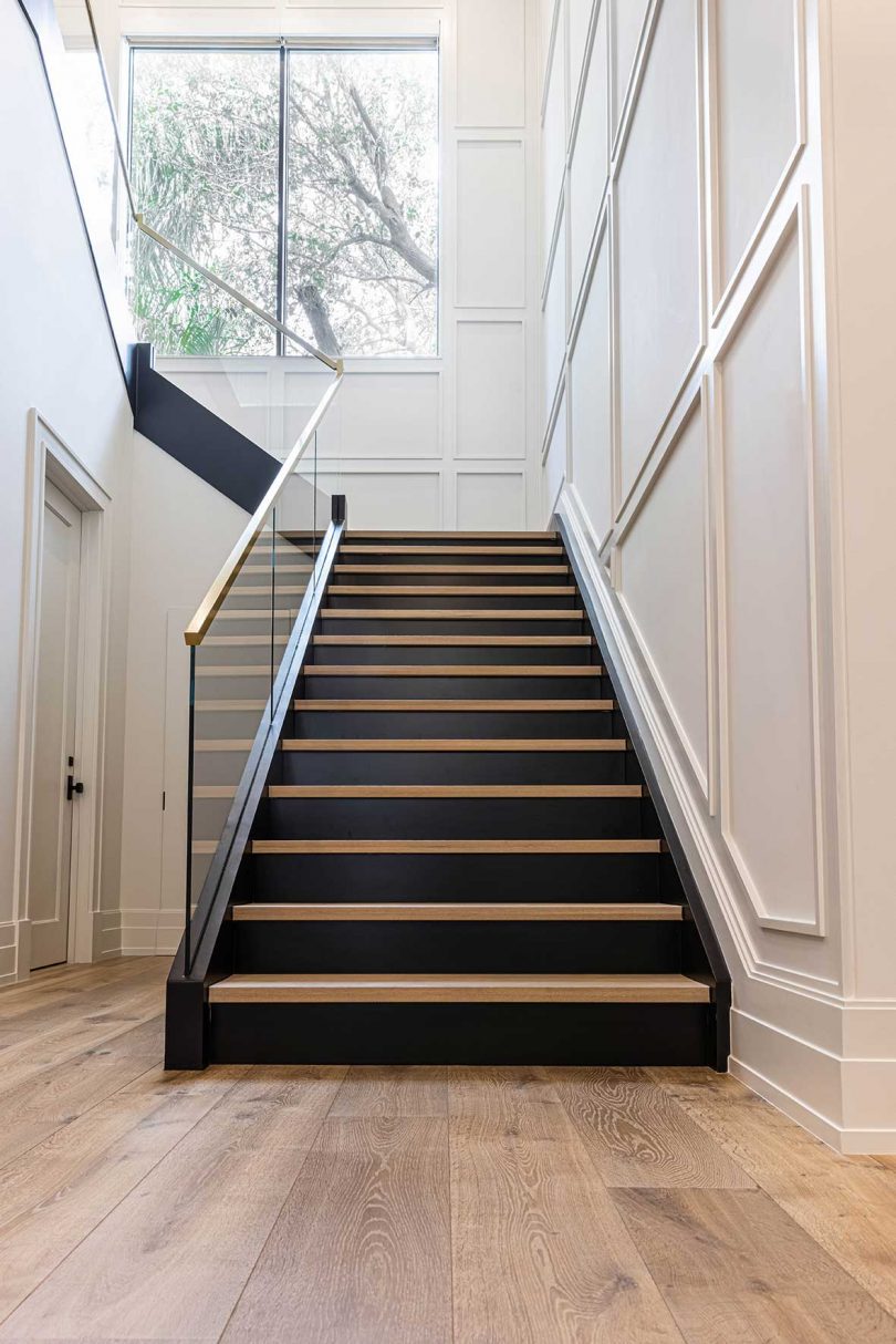 double height staircase with white walls and wood stair treads and glass railing