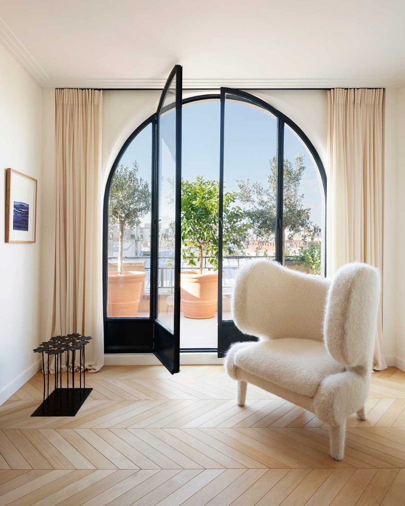 modern living space with cream chair and arched windows looking out to Paris