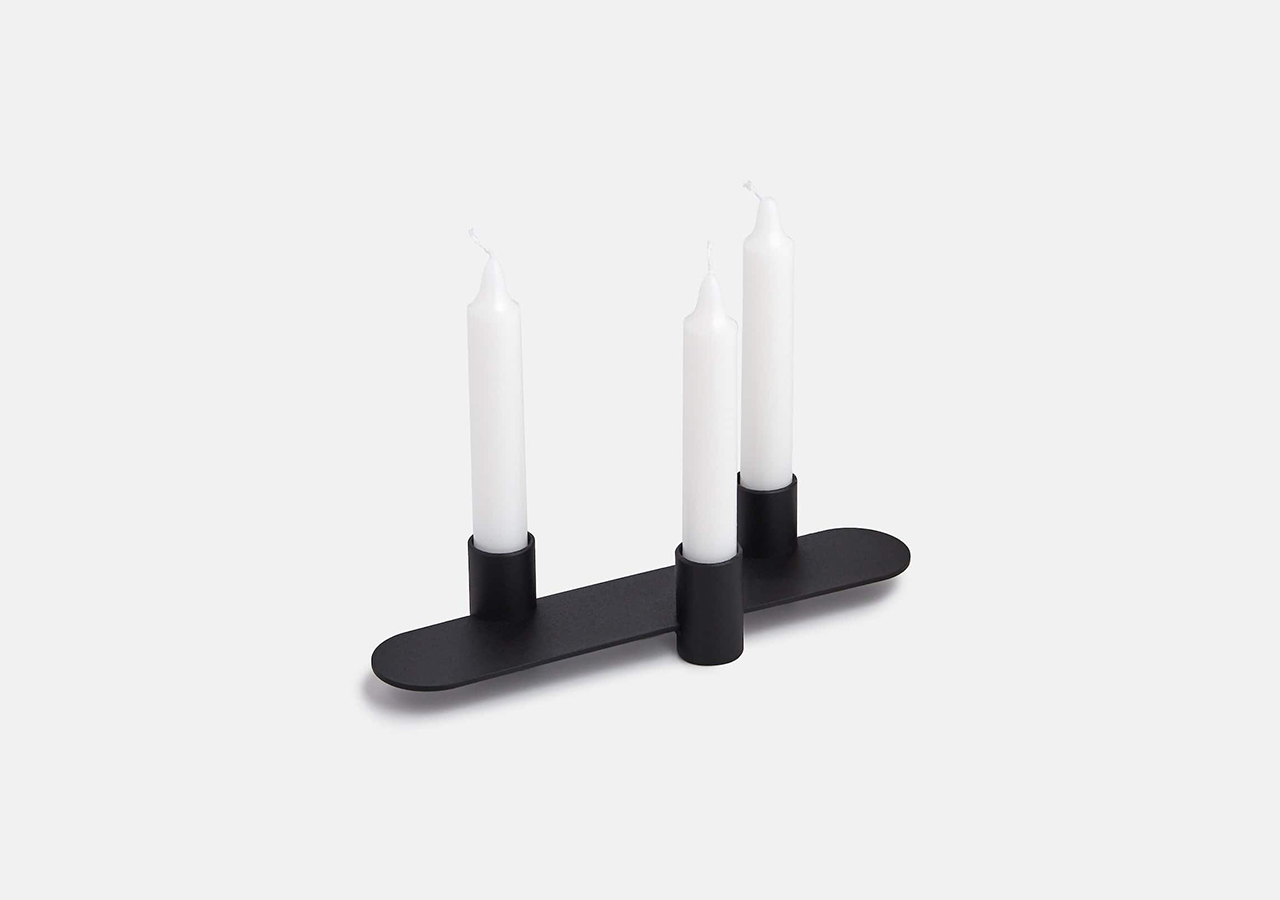 Bristol small candleholder in black with 3 white tapered candles inside, on a light grey background