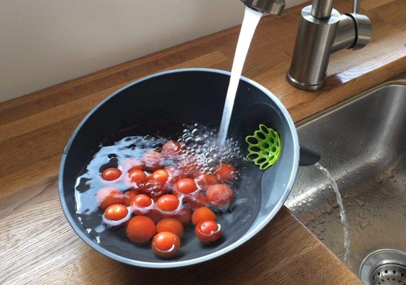 anton strainer bowl with cherry tomatoes inside being rinsed into the sink