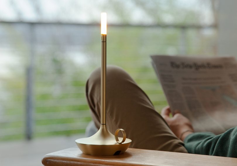 graypants, inc. wick brass portable candlelight on a side table with someone reading in the background