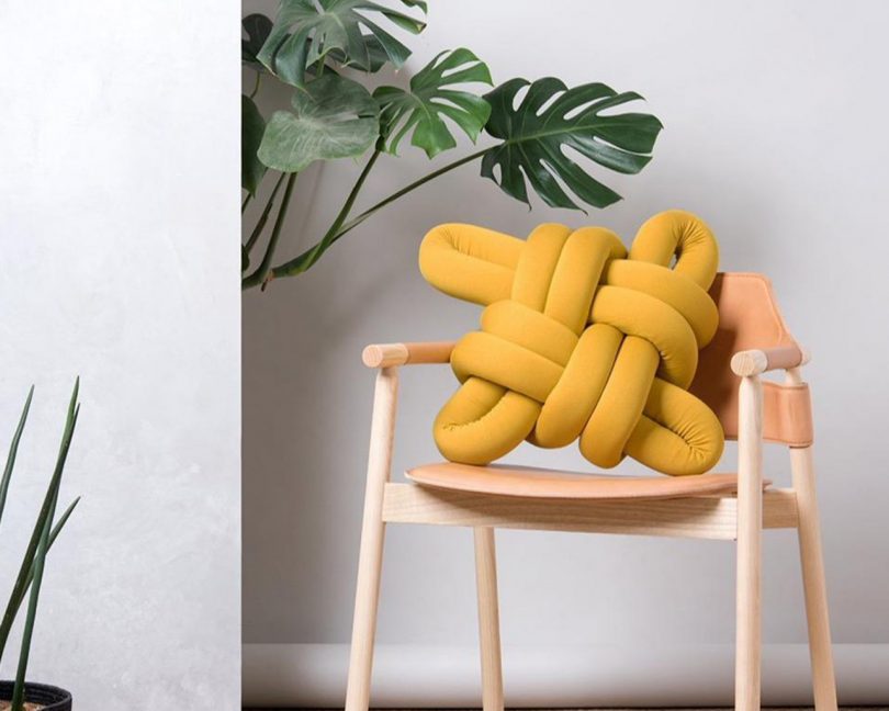 mustard cotton knot pillow by knots-studios on a wooden chair next to a houseplant