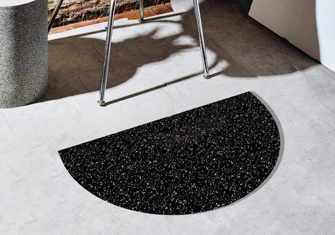 Speckled black half circle mat by slash objects on the ground next to a chair