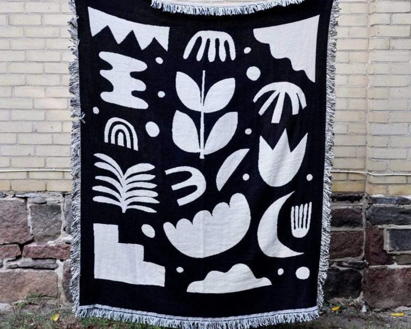 swell made co. botanical throw blanket being held up in front of a brick wall