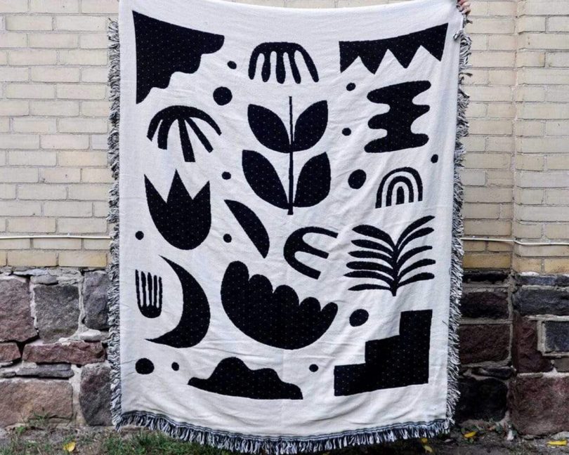 swell made co. botanical throw blanket being held up in front of a brick wall