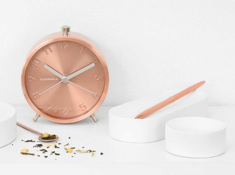 round copper alarm clock on white surface with white desk accessories