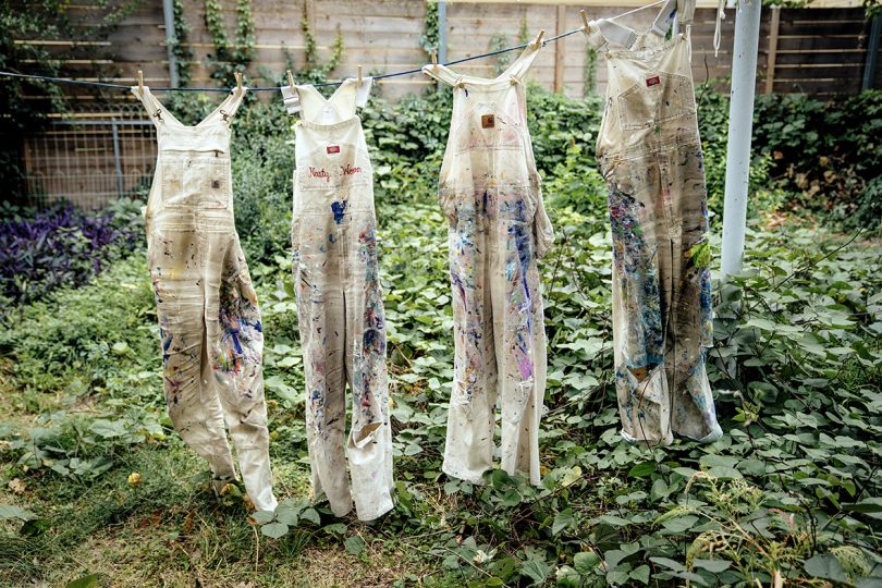 four pairs of paint covered overalls hanging on a clothesline