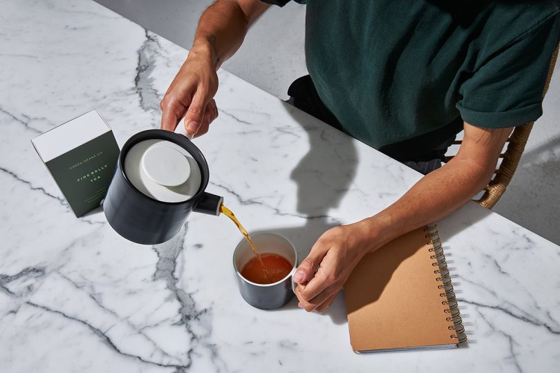 overhead image of person pouring a cup of tea from a black and white teapot over a marble countertop