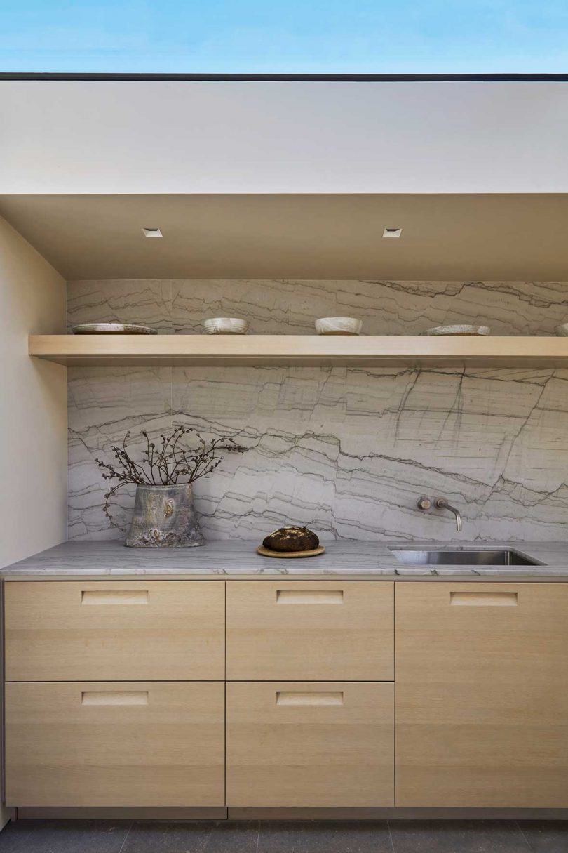 closeup of minimalist kitchen with light wood cabinets and marbled backsplash