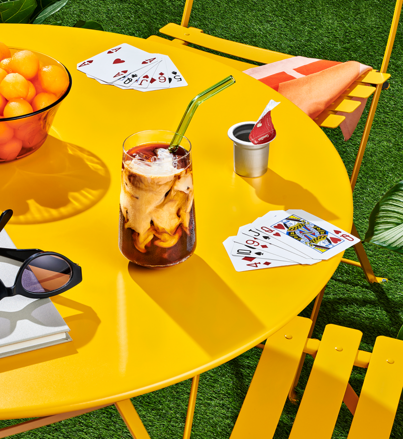 iced coffee in glass with straw sitting on bright yellow styled patio table with two chairs