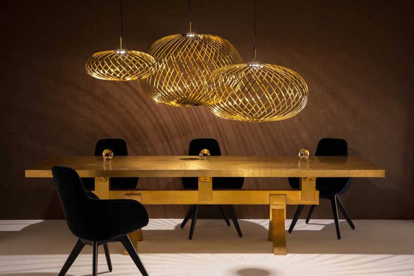 darkened room with solid brass table, black chairs and three brass pendants