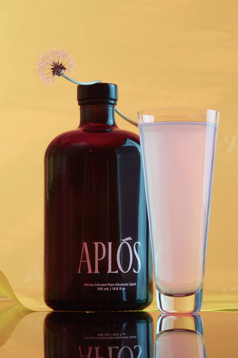brown bottle labeled APLOS next to tall cocktail glass filled with pink liquid
