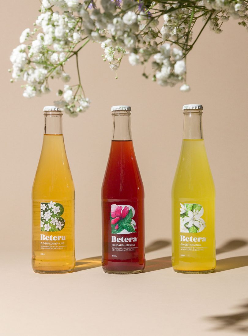 three tall glass beverage bottles filled with colorful liquid with overhanging branch of white blossoms