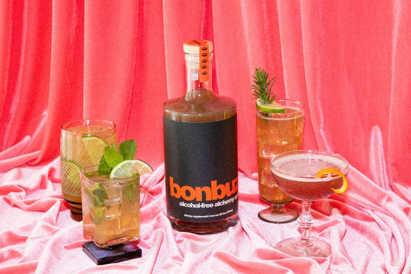 bottle with black label reading bonbuz next to cocktails in front of pin backdrop