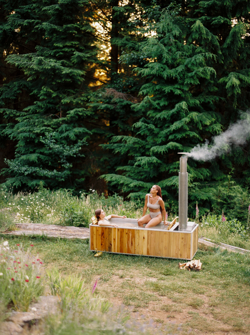 wood burning hot tub in an open green space with two women