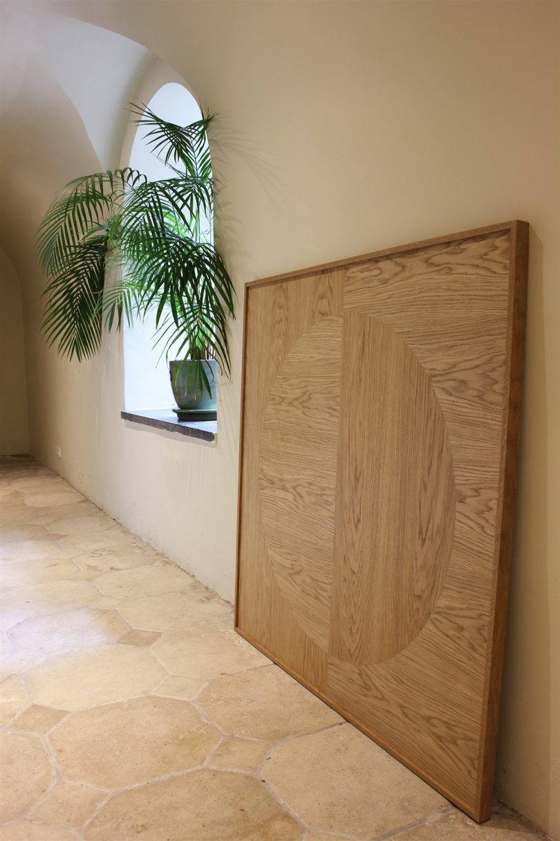 wood marquetry art leaning against wall near potted palm