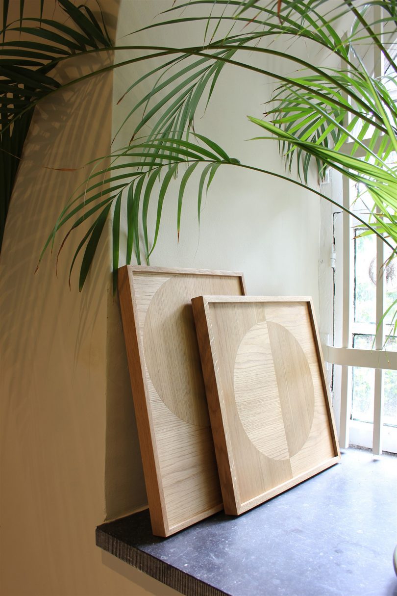 wood marquetry art leaning against wall near potted palm