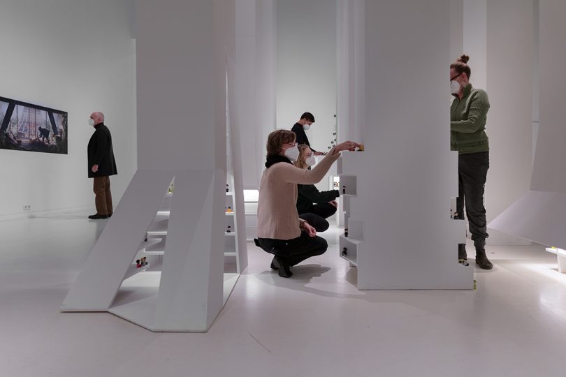 visitors inside interactive exhibition with all white surfaces and small figurines representing people