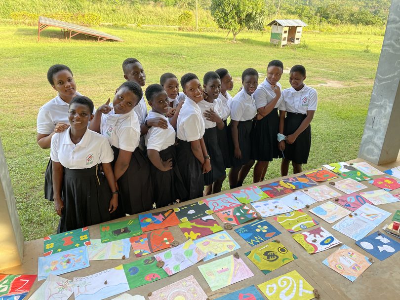 group of schoolgirls gathered in front of their own colorful sketches