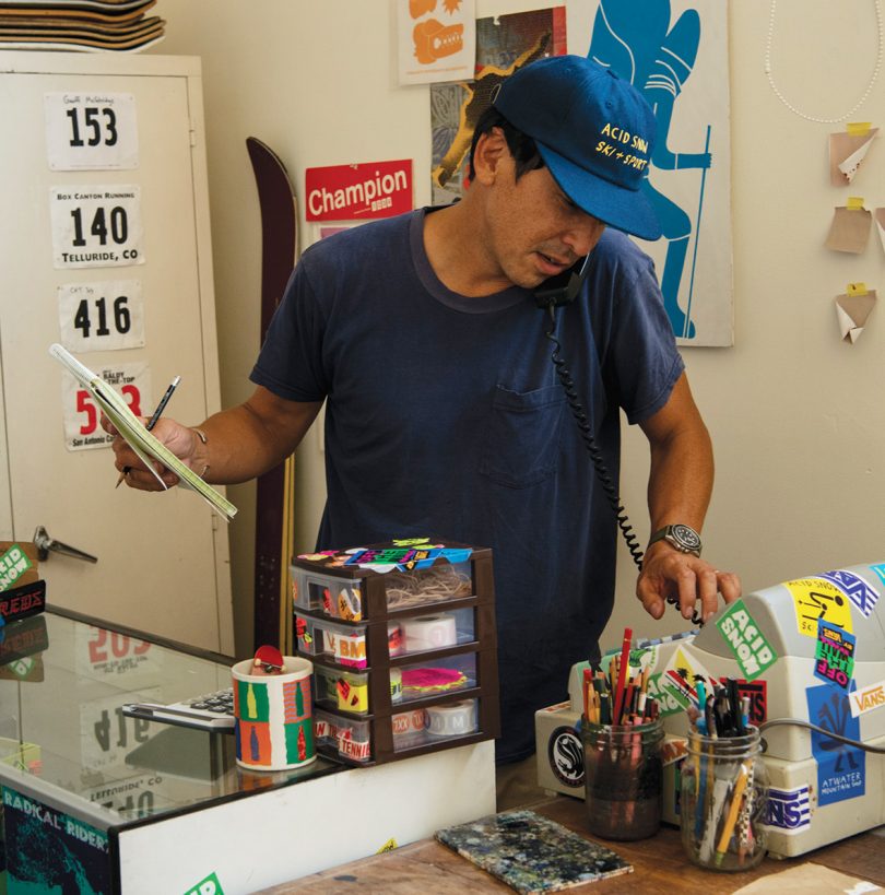 Geoff McFetridge holding pen and paper at a skate shop cash register.