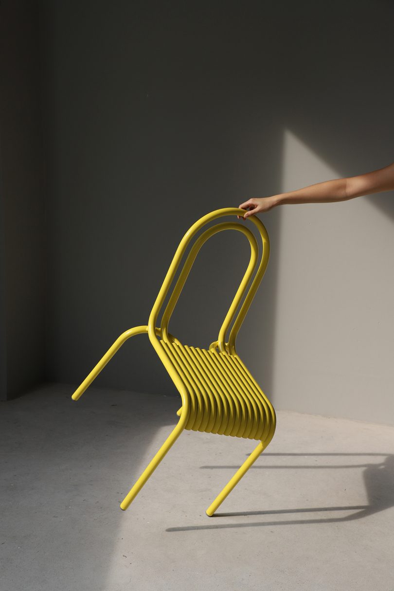 light-skinned arm holding tipped yellow outdoor dining chair