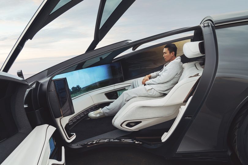 Young Asian man seated inside Cadillac Innerspace car behind large wraparound panel screens.