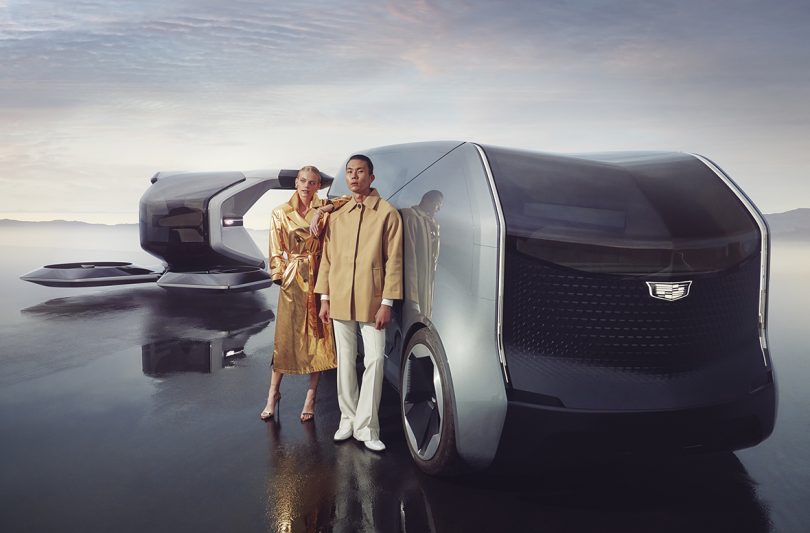 Young White woman with blond hair and young Asian man with short cropped hair both wearing yellow jackets standing in front of Cadillac concept vehicles.