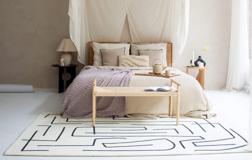 bed with lavender and white bedding, bench, and black and white rug