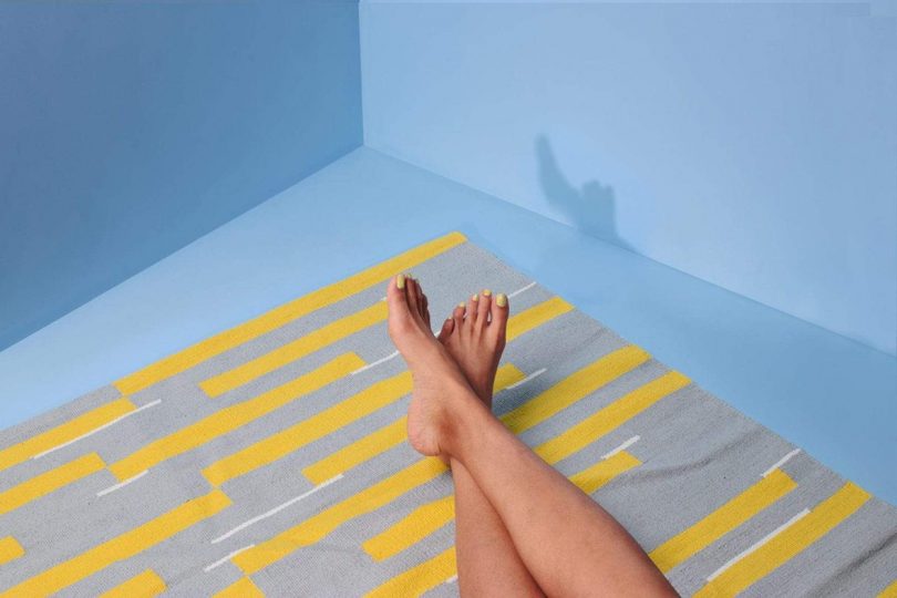 blue and yellow throw rug in light blue space with person's legs