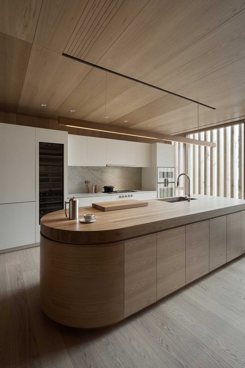 angled view of modern kitchen with long rounded edge island and wood ceiling