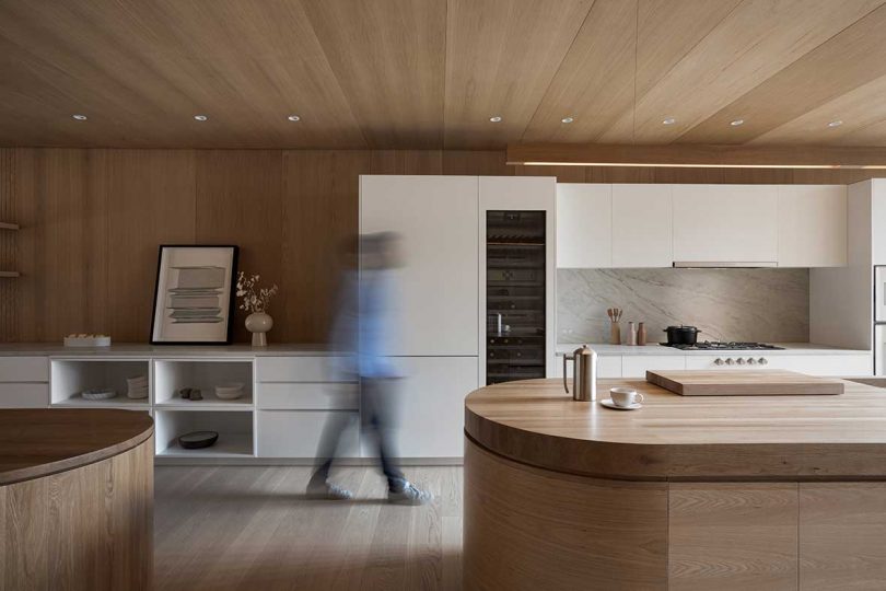 man walking in modern kitchen with white cabinets and wood clad rounded island