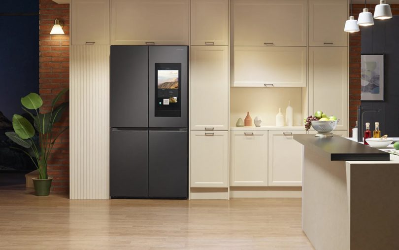 Black 4-door refrigerator with large smart screen display on right upper door in all white kitchen setting.