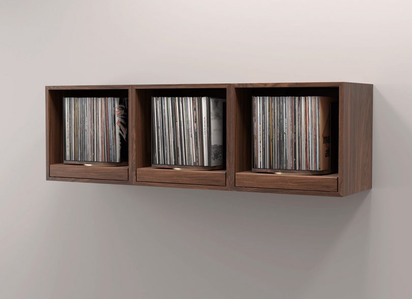 Three rpm record storage units in walnut finish wall mounted side-by-side as one continual display with records in each.