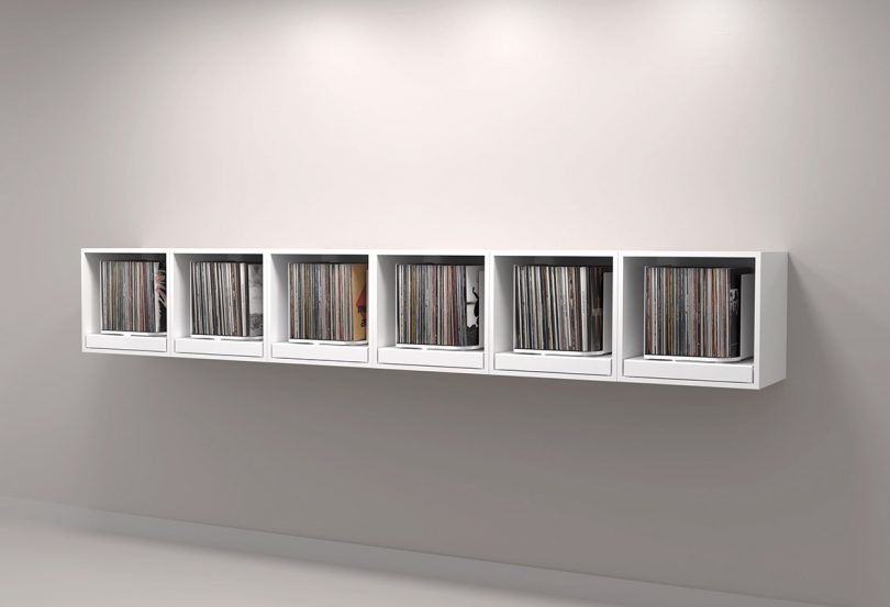Six white rpm record storage units wall mounted side-by-side as one continual display.