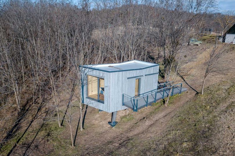 elevated view of tiny cabin on stilts surrounded by trees in winter