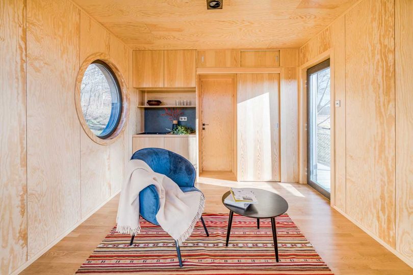 interior view of tiny cabin with wood panel walls and round window with minimal furniture