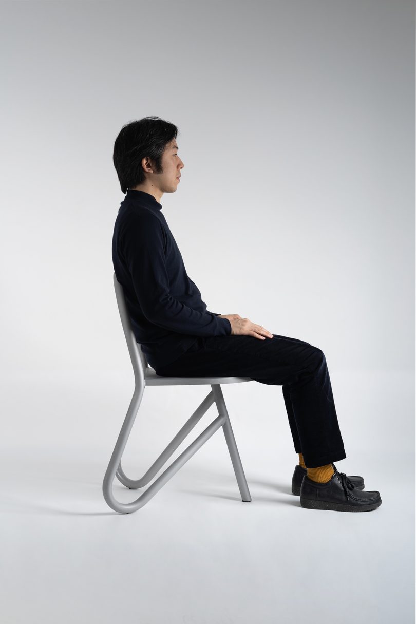 man wearing all black and sitting in profile of tubular chair